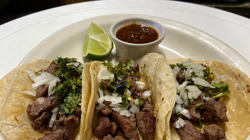Tacos De Carne Asada · Three tacos filled with grilled seasoned carne asada, cilantro, and onions. Served with refried beans, rice, and green sauce.
