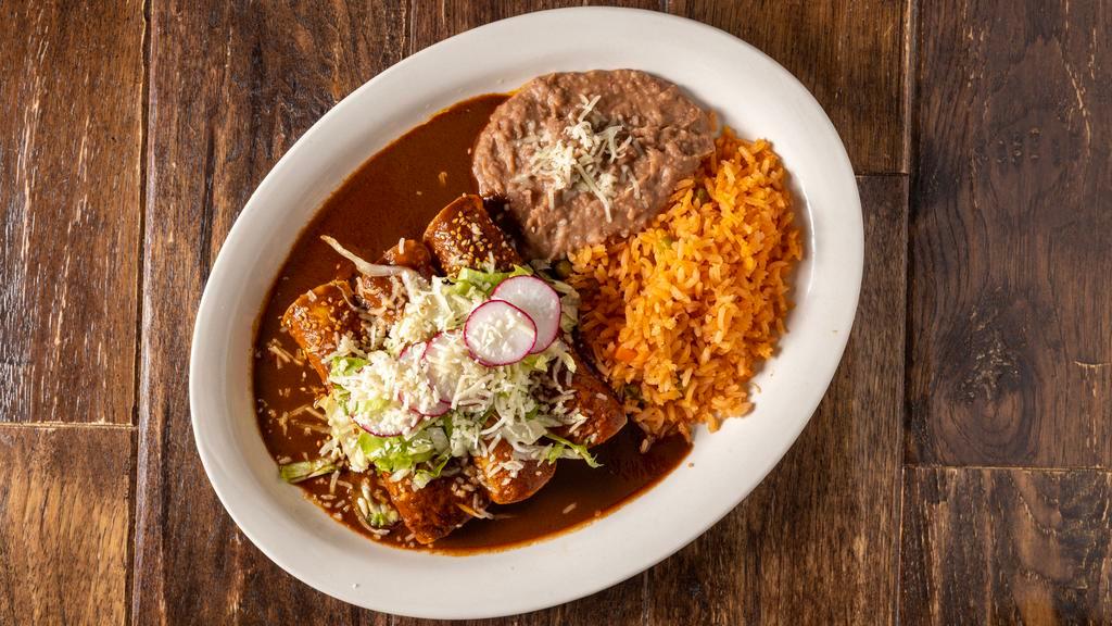Enchiladas De Mole Poblano · 3 enchiladas with mole poblano sauce topped with lettuce, onions, radishes, fresh cheese, rice and beans.