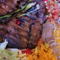 Carne Asada · Slices of thin rib-eye steak served with rice, beans, slices of onion, avocado, lettuce, pic...