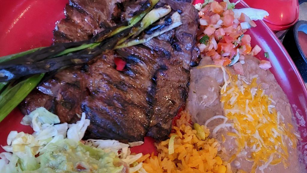 Carne Asada · Slices of thin rib-eye steak served with rice, beans, slices of onion, avocado, lettuce, pico de gallo, and three corn tortillas.