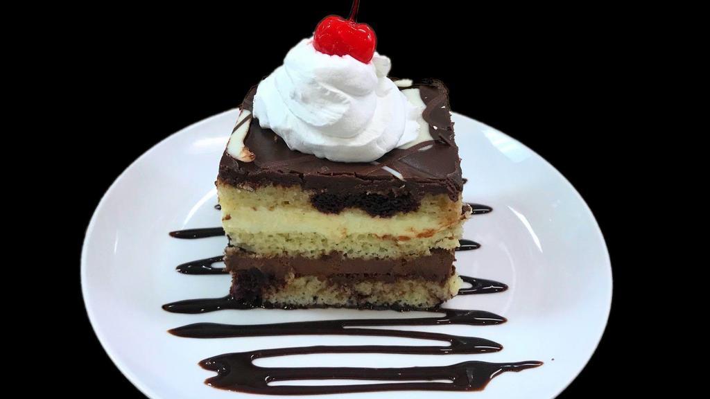 Chocolate Mousse Cake · White and dark chocolate mousse floating between three layers a marble white and dark chocolate cake topped with a swirl of white and dark chocolate ganache. Decorated with chocolate syrup, whipped cream and a cherry on top.