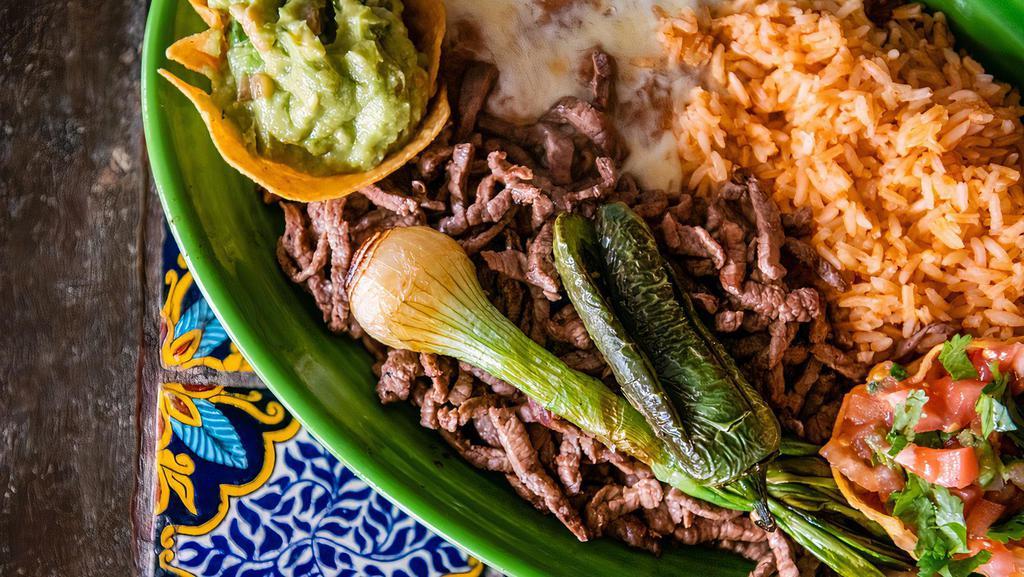 Carne Asada · Marinated top sirloin steak topped with grilled onions. Served with rice, beans, guacamole salad, and hot tortillas.