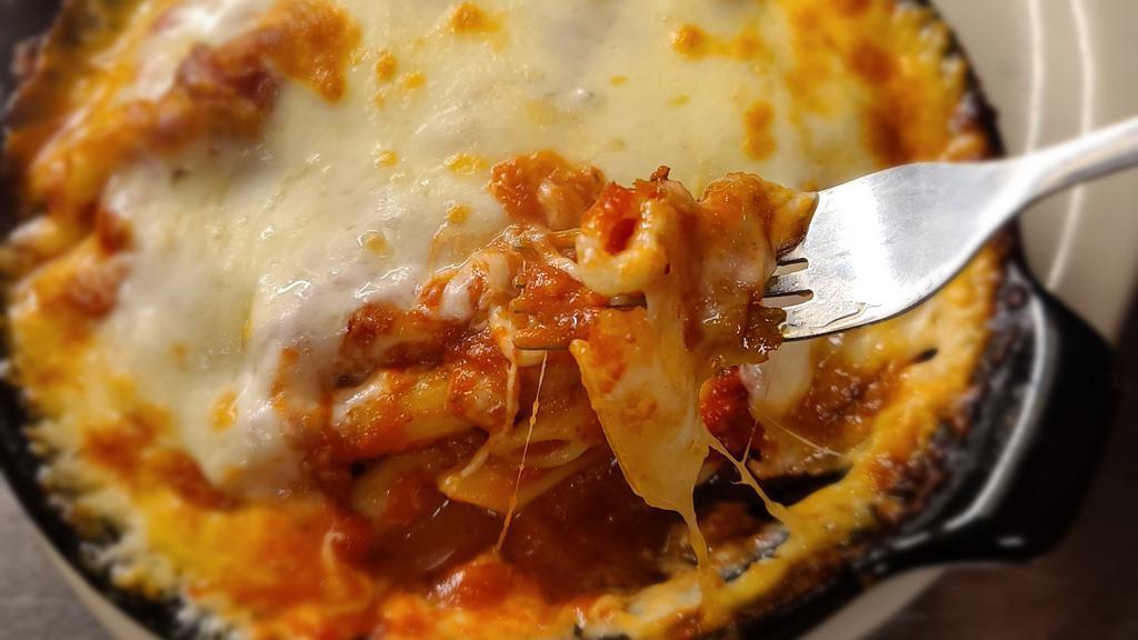 Cheesy Baked Ziti · Our take on a simple comfort food. 
We take our penne pasta, add our delicious marinara sauce, some minced garlic, and heap the cheese on top. Then we bake it until the cheese is golden and oh so delicious.