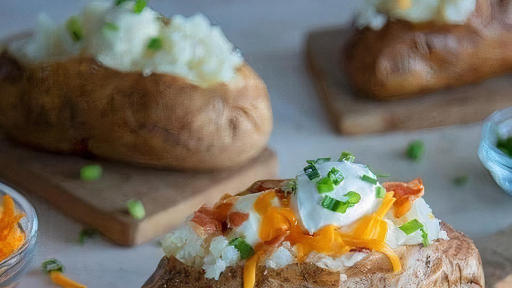 Loaded Baked Potato · Baked potato loaded with butter, sour cream, chopped bacon, and cheddar cheese, then garnished with chopped green onions.
