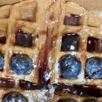 The Blue Drip Waffles · One blueberry waffle covered with blueberries and blueberry syrup.