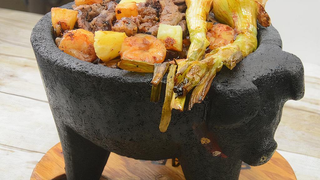 Molcajete Tlaquepaque · A hot stone bowl filled with rib-eye steak, chicken, shrimp, bell peppers, onions, chunks of pineapple, and honey pasilla sauce, topped with shredded cheese. Served with rice, beans with cheese, and tortillas.
