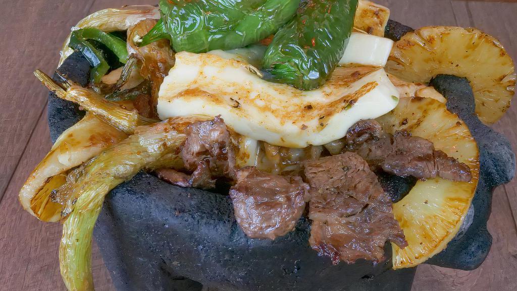 Molcajete Special · A hot stone bowl filled with rib-eye steak, chicken, shrimp, bell peppers, slice of pineapple, and salsa verde, topped with Mexican grilled cheese. Served with rice, beans with cheese, and tortillas.