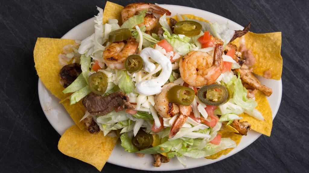 Fajita Nachos Mixtas · Bed of tortilla chips with beans your choice of two meat with cooked tomatoes onion and green pepper with lettuce sour cream and guacamole and cheese dip on top.