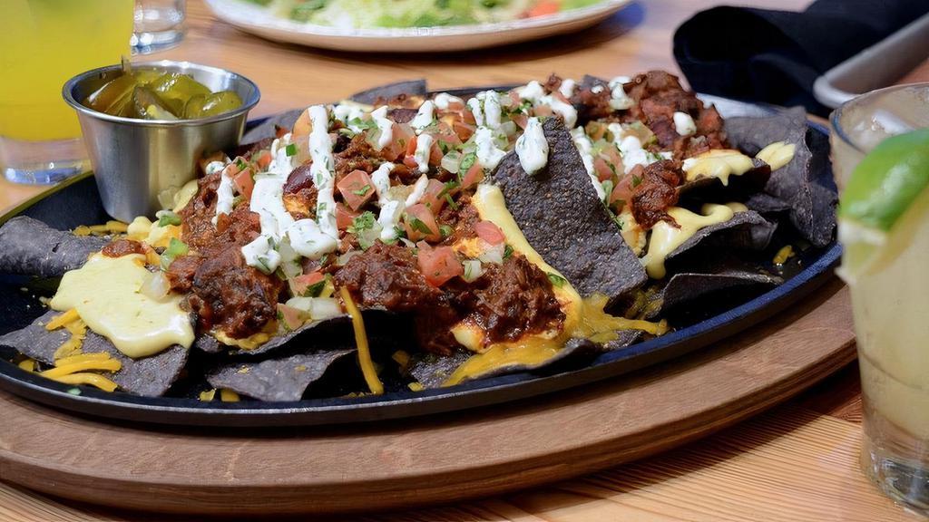Brisket Chili Nachos(Xl) · Gluten Free blue corn tortilla chips topped with Smoked Queso, brisket chili, Sharp Cheddar, House-made pico de gallo and finished with cilantro-lime sour cream served with candied jalapeños on the side.