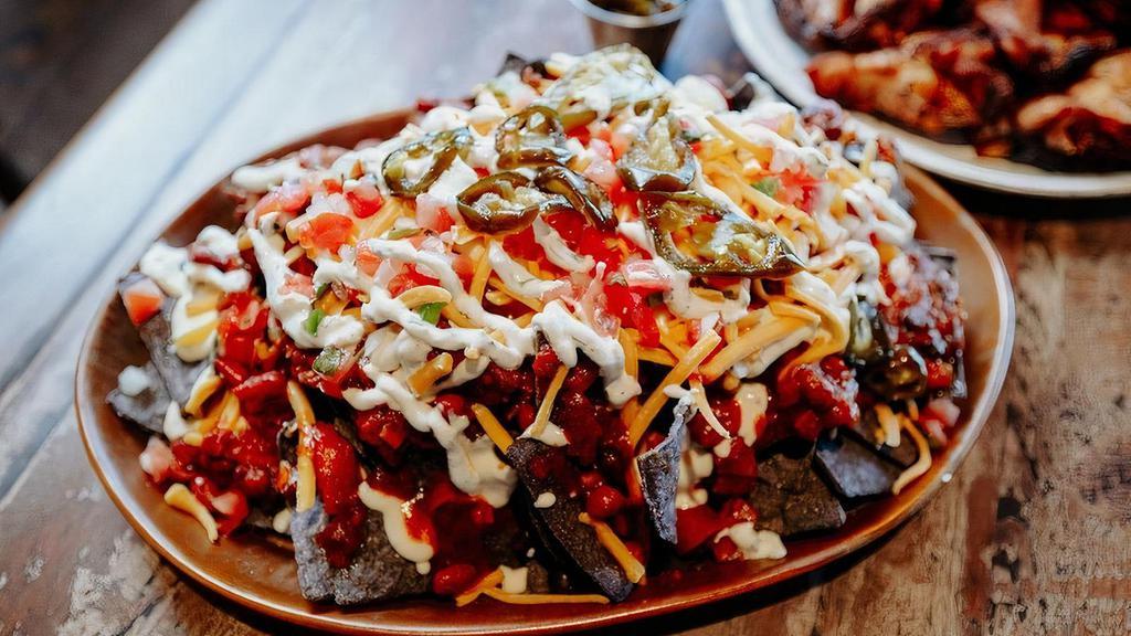 Brisket Chili Nachos(Half) · Gluten Free blue corn tortilla chips topped with Smoked Queso, brisket chili, Sharp Cheddar, House-made pico de gallo and finished with cilantro-lime sour cream served with candied jalapeños on the side.