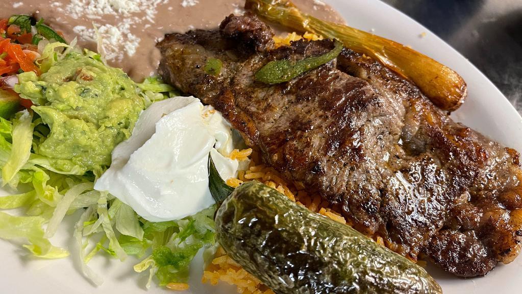 Carne Asada/Grill Steak · Tenderly grilled ribeye steak thin slice and served with rice, refried pinto beans, fresh guacamole, lettuce and pico de gallo accompanied with your choice of flour or corn tortillas.