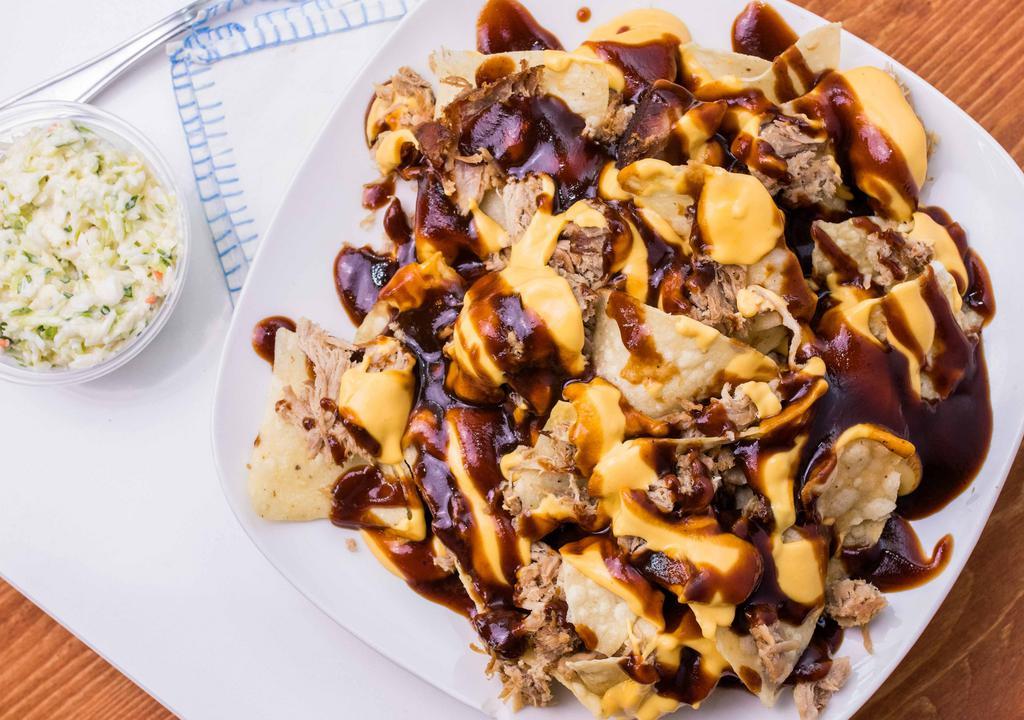 Full Bbq Nachos · pile of homecooked chips  smothered in creamy queso with a mound of smoked bbq meat on top .