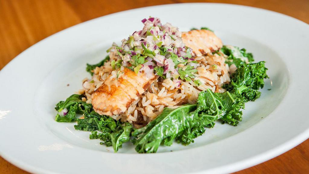 Samkeh Harra · Pan-seared salmon filet topped with tahini sauce, cilantro, mint, onions, and a hint of jalapeño, served with sautéed kale and Sitti rice.