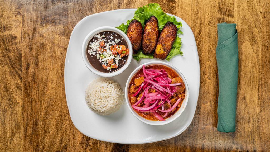 Cochinita Pibil · Cochinita is a traditional Mexican pork dish from the Yucatan peninsula. Preparation involves marinating the meat in acidic juices seasoned with annatto(achiote) and roasting the meat while it is wrapped in banana leaf. Served with rice, black beans and sweet plantains.