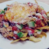 Chilaquiles · Tortilla strips simmered in red sauce, served with melted cheese, shredded chicken and a fri...