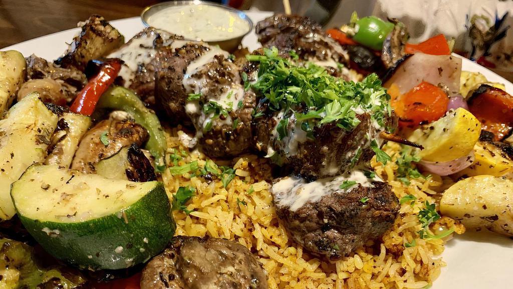 Beef Kebab Platter Lunch · Beef kebab skewers marinated in organic thyme, toasted sesame seeds, olive oil, and red wine vinegar, then char-grilled to order and served on a bed of basmati rice with grilled vegetables and a side of homemade tzatziki sauce.