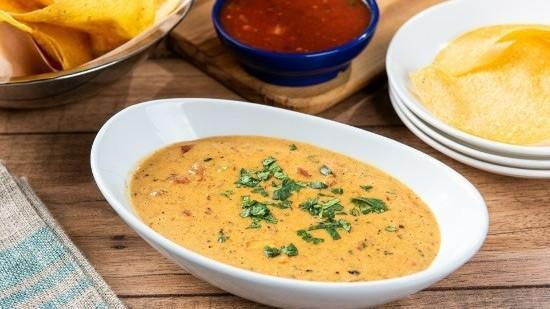 Smoky Queso · Our signature queso kicked-up with roasted red chile tomatillo salsa and cilantro.