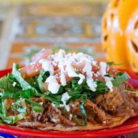 Tinga Sope · Open face home-made corn tortillas smothered with beans. Topped with lettuce, tomatoes, chee...