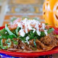 Carnitas Sope · Open face home-made corn tortillas smothered with beans. Topped with lettuce, tomatoes, chee...