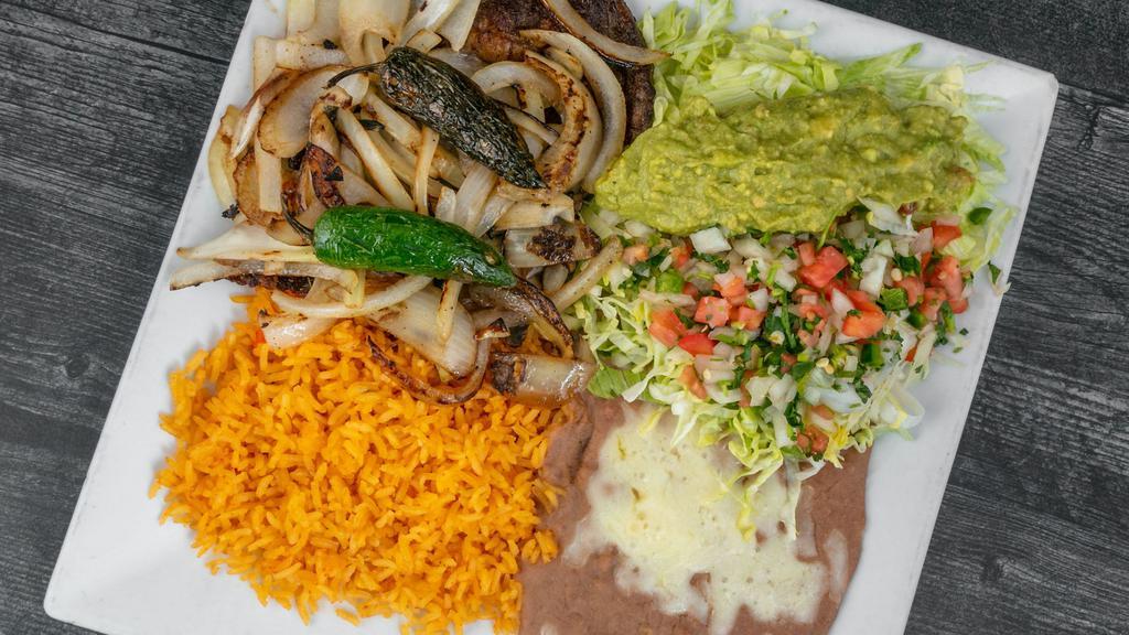 Carne Asada · Thin sliced rib-eye steak topped with fresh jalapeños, avocado, grilled onions and served with rice, beans, guacamole salad and tortillas.