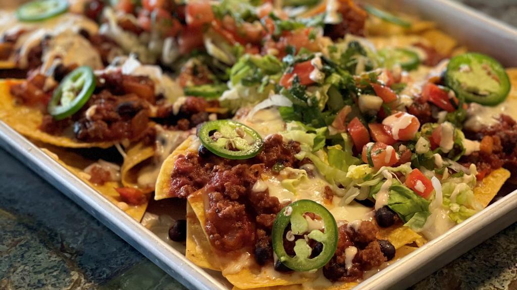 Chicken Nachos · crispy nachos with roasted chicken, smothered with creamy queso, pico de gallo, shredded lettuce, jalapeños and chipotle crema.