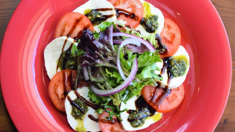 Caprese Salad · Fresh mozzarella, tomatoes, spring mix, thin sliced red onions, homemade pistachio pesto, and balsamic dressing.