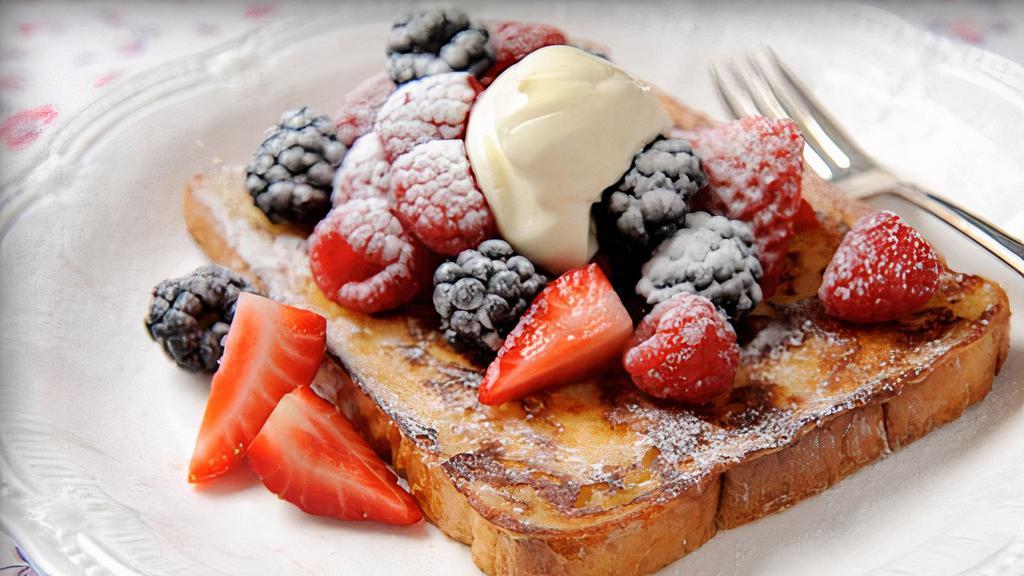 Berry French Toast · Three slices of thick, egg-washed challah bread topped with fresh blueberries and strawberries, and served with syrup and powdered sugar.