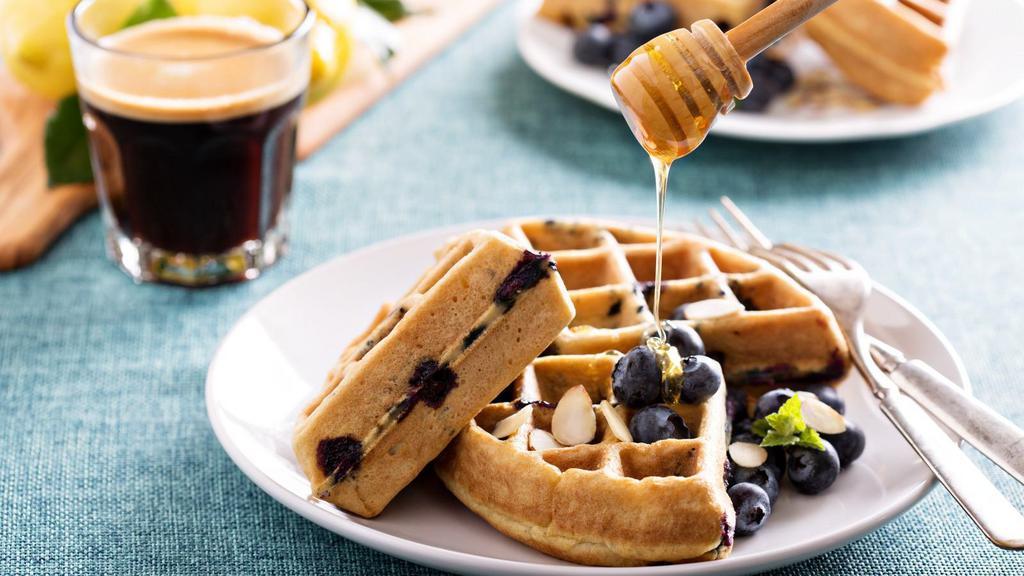 Blueberry Belgian Waffles · Crisp cake of batter baked in a waffle iron topped with fresh blueberries, served with a side of butter and syrup.