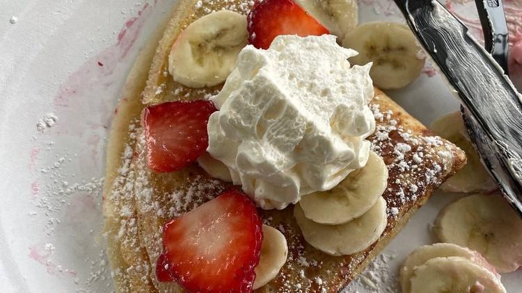 Strawberry-Banana Crepe · Two crepes filled with homemade strawberry cream, topped with fresh strawberries, banana slices, whipped cream and powdered sugar.