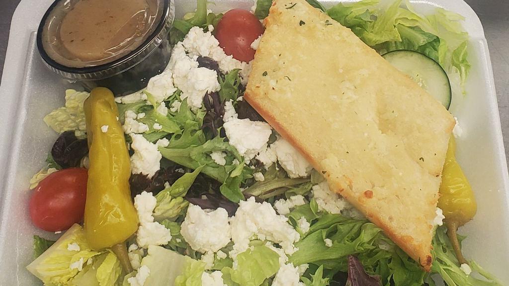 Greek Salad · Mixed greens topped with Feta, tomatoes, cucumber, red onion, black olives, pepperoncini, and Greek dressing. Served with garlic bread.