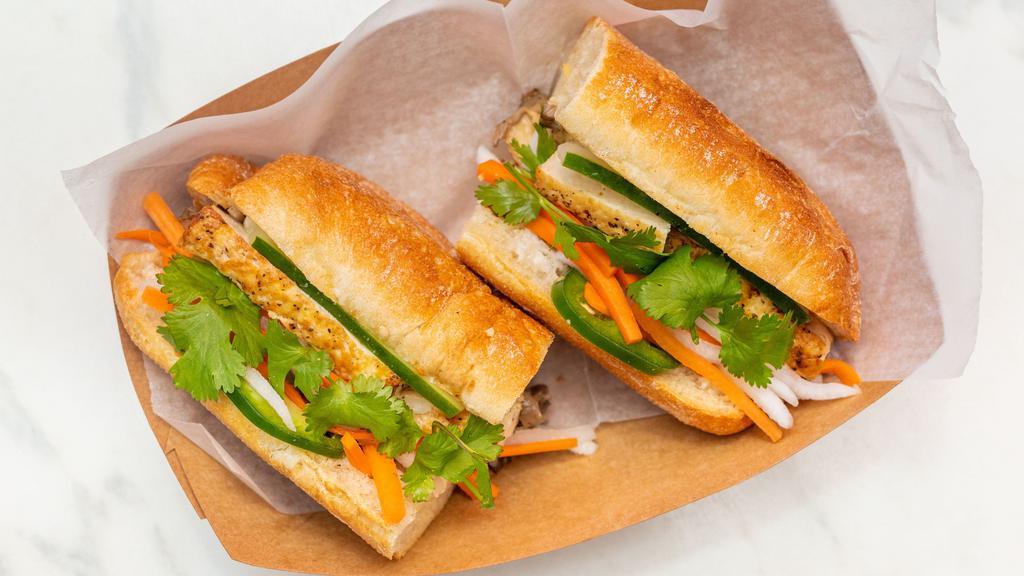 Banh Mi - Tofu + W. Mushroom · Golden-fried tofu & pan-seared garlicky wild mushrooms in a delicately crispy French baguette layered with vegan mayo, Maggi, onions, jalapenos, cucumbers, fresh cilantro, and pickled daikon & carrots | Vegan | Allergens: soy, wheat