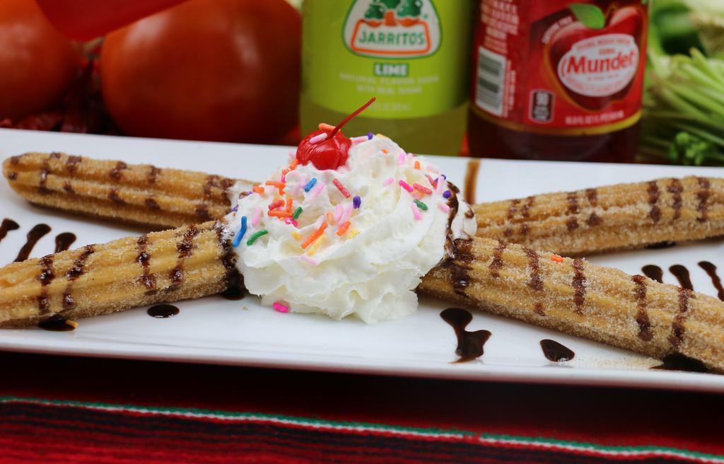 Churros · Two churros served with chocolate sauce, whipped cream and sprinkles.