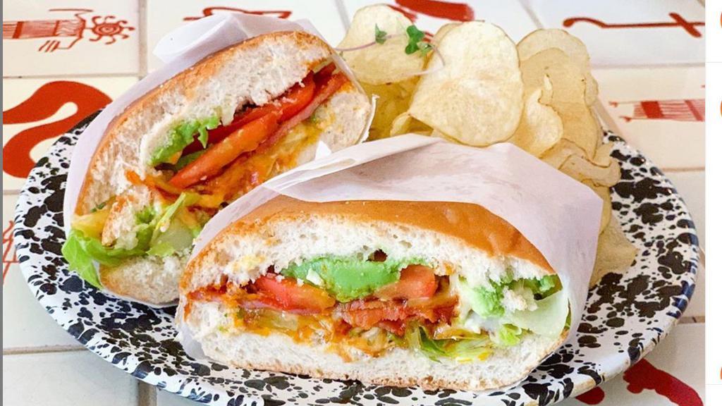 Hawaiian Torta · torta bread filled with smoked ham adobo, pineapple, melted Oaxaca cheese, lettuce, tomatoes, mayo, onions, avocado, & jalapeños served with house made potato chips