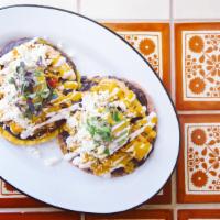 Tostadas De Tinga · Two fried house tortillas topped with refried beans, organic chicken tinga, queso fresco, ca...
