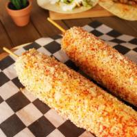 Elotes Street Corn Stick · Buttery whole corn on a stick and smothered in yum yum sauce topped with cotija cheese and s...