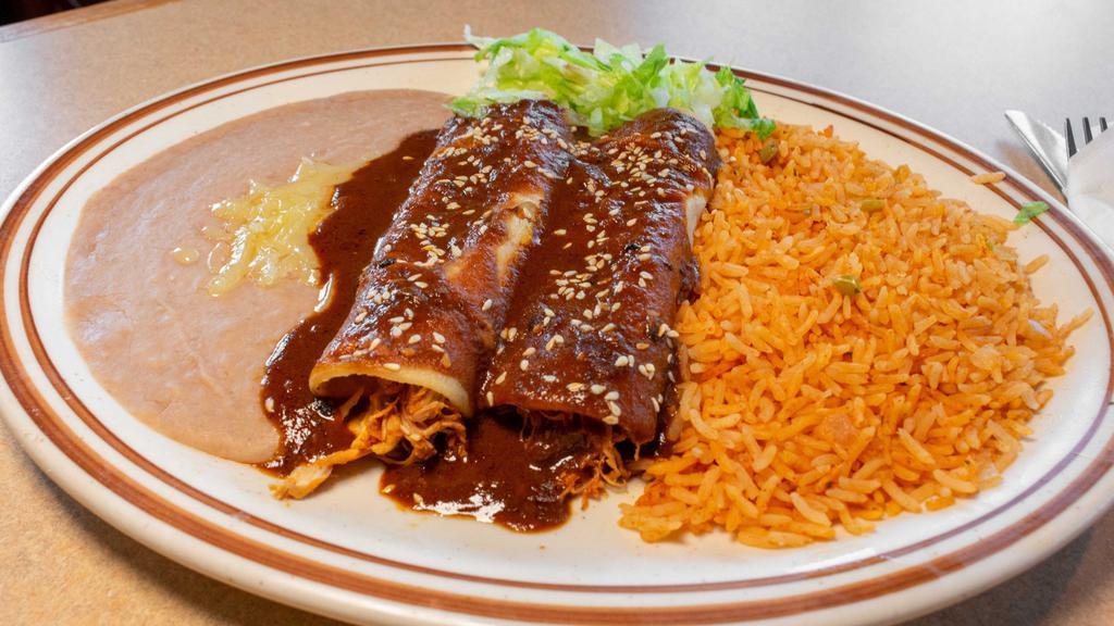 Mole Enchiladas · Contains peanuts. Two corn tortillas stuffed with shredded chicken, and topped with house-made sweet brown mole sauce and sesame seeds. Served with Mexican rice and refried beans.