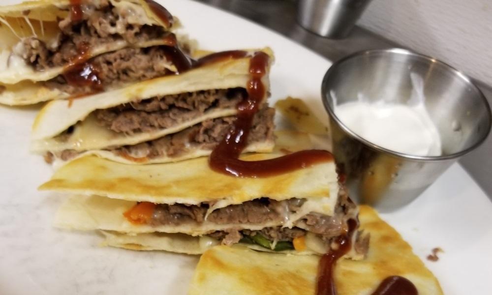 Cheesesteak Quesadilla · Shaved ribeye, caramelized onions and peppers, provolone, fontina cheeses, flour tortillas, black bean, corn relish, BBQ sauce drizzle, sour cream, cheese sauce