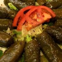 Grape Leaves Appetizer · Plate of six grape leaves stuffed with rice, served on a bed of lettuce with pickles and tom...