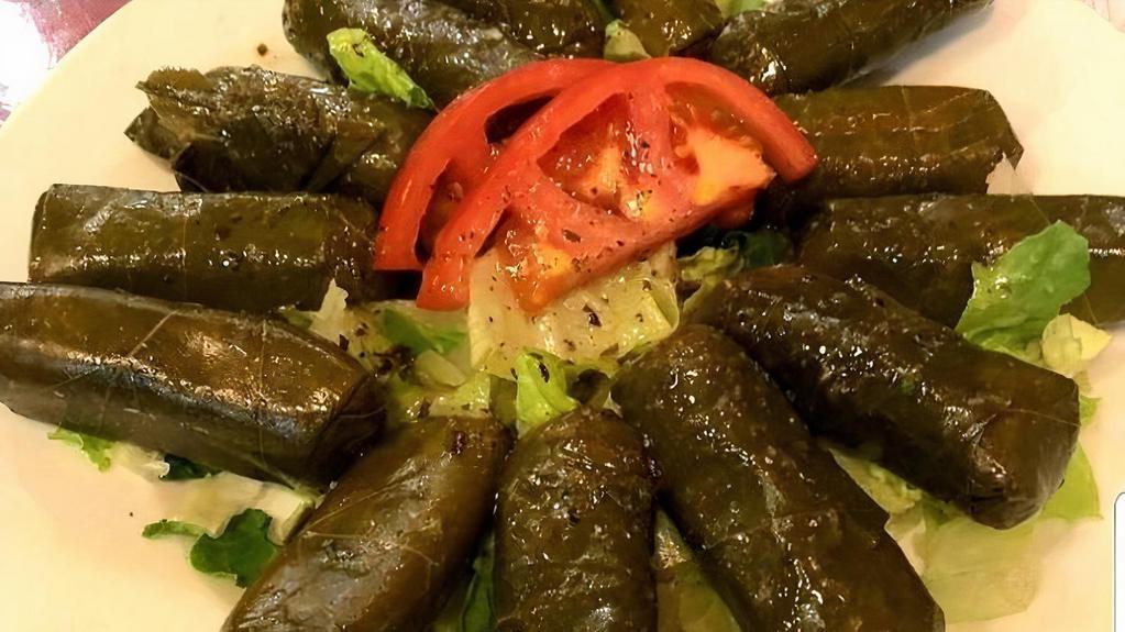 Grape Leaves Appetizer · Plate of six grape leaves stuffed with rice, served on a bed of lettuce with pickles and tomatoes. Topped with a sumac vinegar sauce.