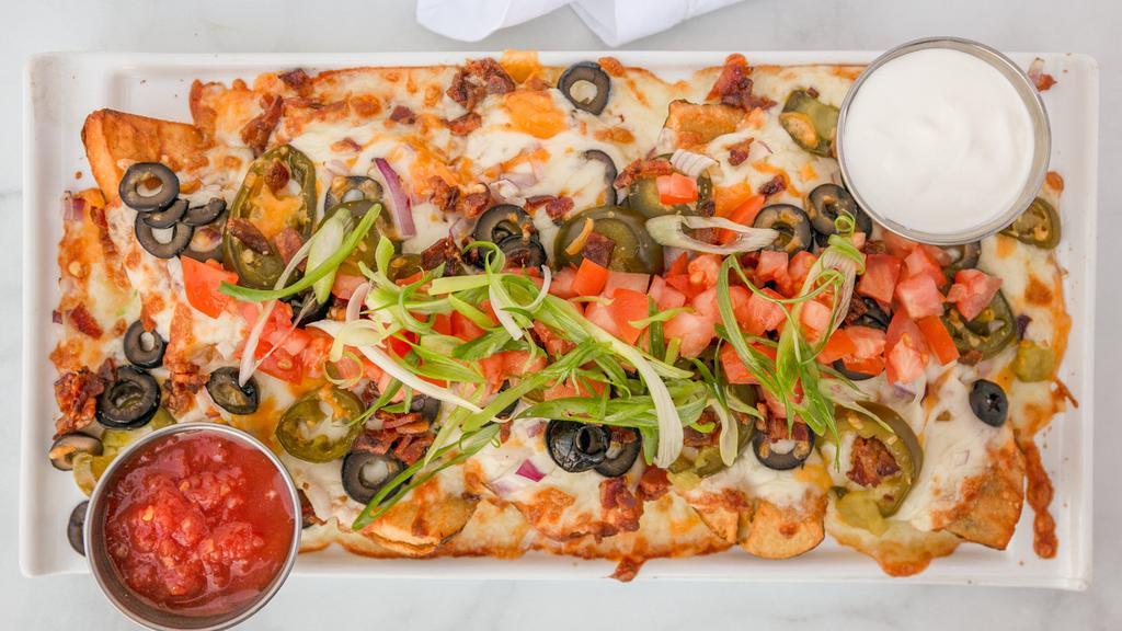 Nacho Potato Skins · Fresh potato nachos loaded with melted cheese, bacon crumbles, black olives, and pickled jalapeños. Finished with fresh diced tomato, scallion, sour cream and salsa.