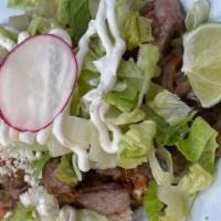 Carnitas Huarache · Crispy pork on a homemade corn tortilla with refried black beans, Oaxaca cheese, lettuce, pi...