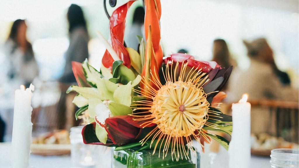Small Tropical Arrangement · Bring your loved one a whole tropical moment by sending them this lush arrangement in a leaf wrapped glass vessel. We'll give them all the aloha vibes. Note: flower selection is based on availability and design time is approx 1-2 hours.