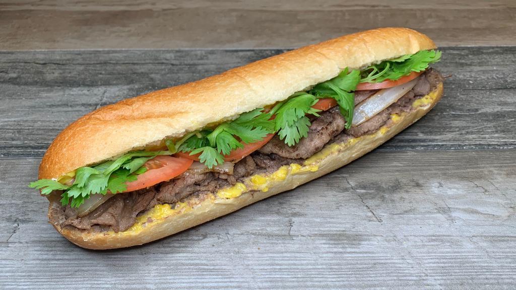 Spicy Steak Banh Mi · Steak banh mi on a soft crunchy roll, with a spread of mayo and pate, fried onion, tomato, and cilantro.