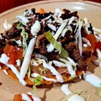 Asada Tostada (Steak) · crispy corn tortilla spread with beans topped with lettuce tomatoes cheese and sour cream.