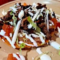 Chorizo Tostada · crispy corn tortilla spread with beans topped with lettuce tomatoes cheese and sour cream.