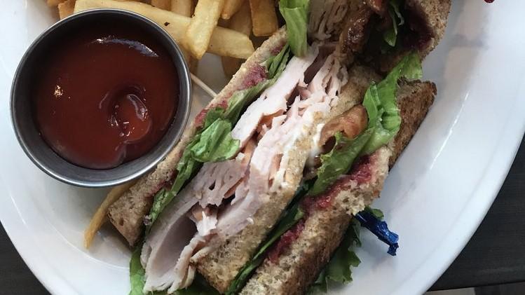 Turkey Club · traditional style turkey club on whole grain bread with hickory smoked bacon, lettuce, tomato and sundried cranberry spread,  served with french fries.