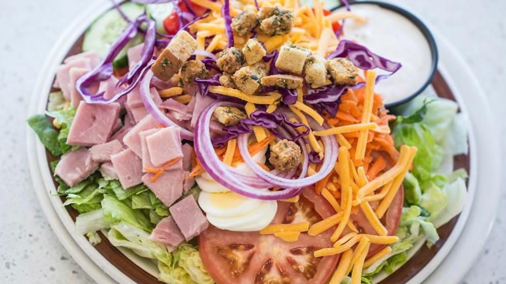Garden Salad · A blend of iceberg and romaine lettuce topped with carrots, cucumber, hard-boiled egg, red peppers, purple cabbage, red onions, shredded cheddar cheese, tomato, our homemade croutons, and your choice of dressing. (similar picture without the ham).