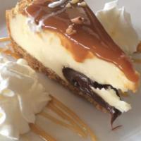 Gourmet Turtle Cheesecake · A generous wedge of new york style cheesecake resting on a thick layer of fudge, covered wit...