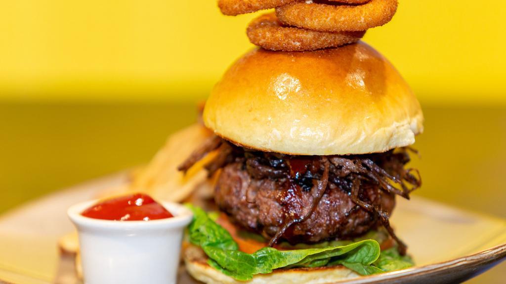 Cowboy Tailgate Burger · Grilled 8oz Burger, Homemade BBQ Sauce, Sliced Smoked Brisket, Topped with Crispy Onion Rings, on a Toasted Brioche Bun, Served with Fries.
