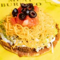 Super Tostada · A flat crisp, deep fried corn tortilla covered with refried beans, a scoop of 100% ground be...